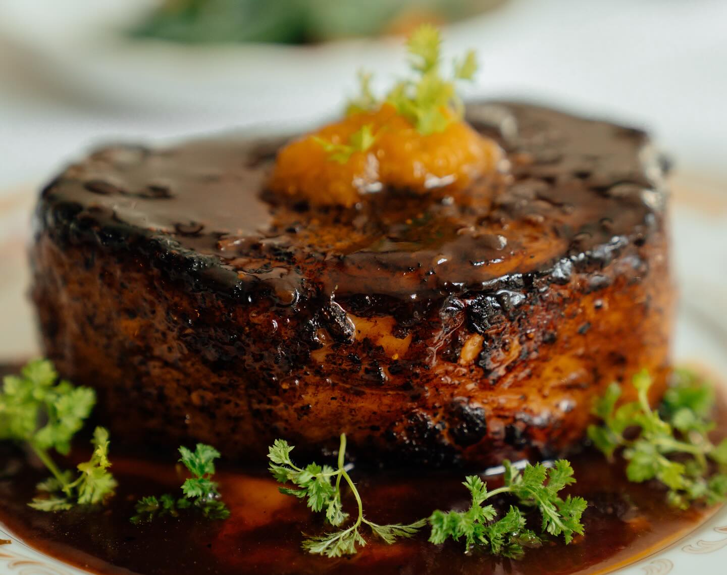 A braised beef course glazed in dark sauce on a white plate