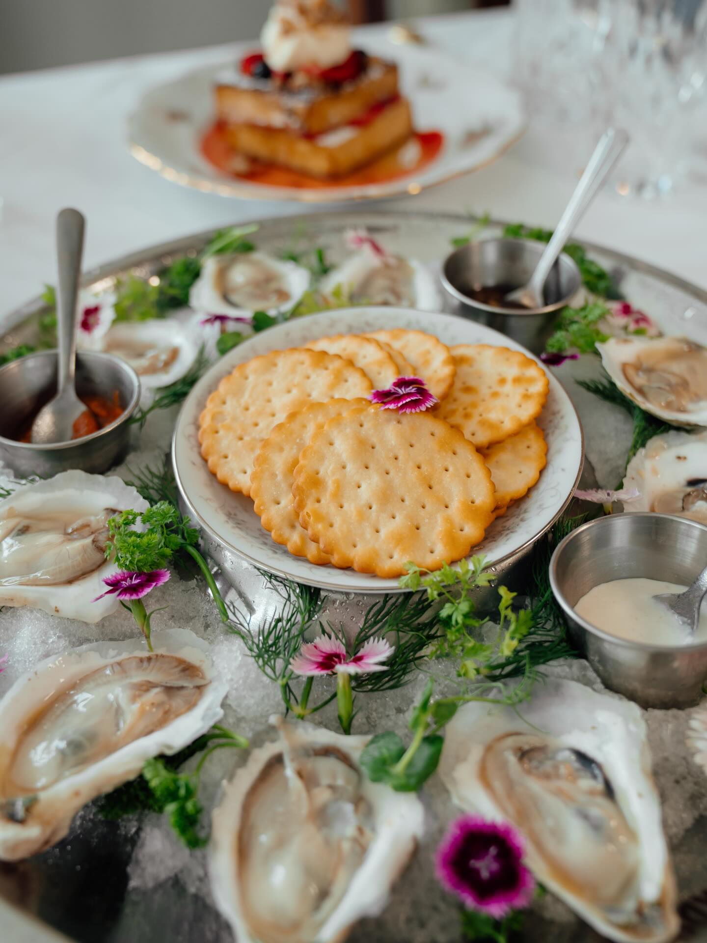 A platter of oysters on ice with crackers and edible flowers