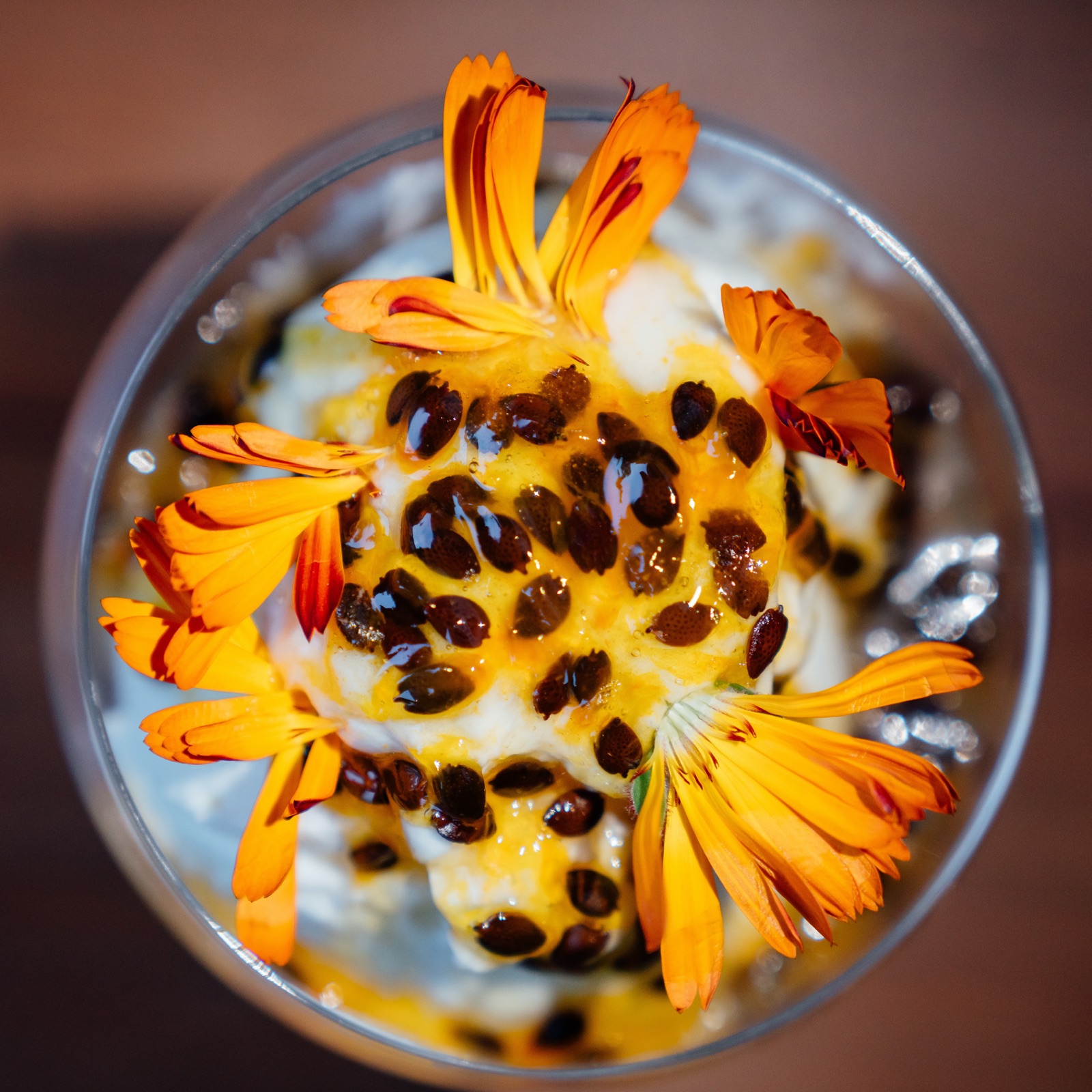 A dessert in a glass topped with passionfruit and orange marigold petals