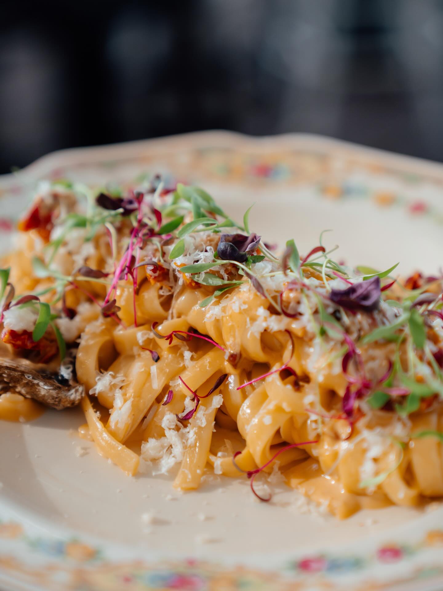 Pasta in a cream sauce with herbs and petals on floral china